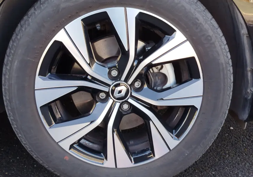 Gros plan sur la jante alliage bicolore noire et argent avec logo Renault au centre, roue d'une Clio 1.6 E-Tech noir étoile.