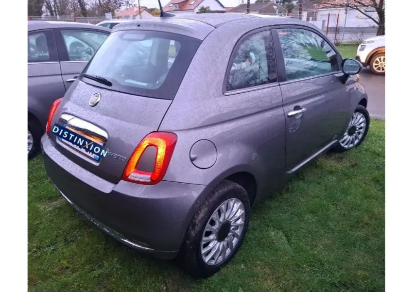 Vue 3/4 arrière droite d'une FIAT 500 2022 gris Electroclash avec feux arrière allumés sur pelouse humide.