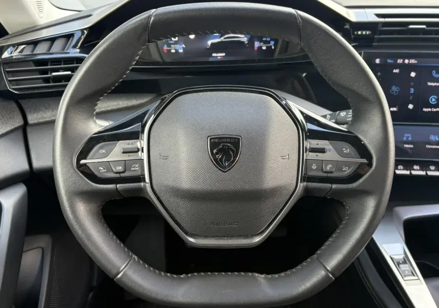 Vue rapprochée du volant cuir noir de la Peugeot 308 2024 avec commandes intégrées et tableau de bord numérique.