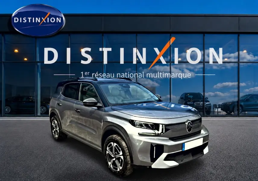 Vue 3/4 avant droite d'un Citroën C3 Aircross gris mercury avec jantes alu et toit noir devant un showroom Distinxion.