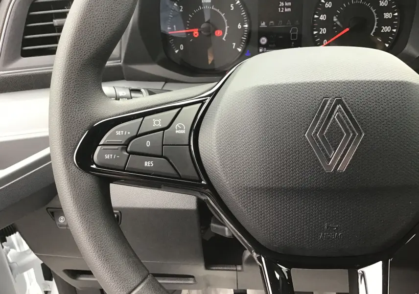 Gros plan sur le volant noir du Renault Master blanc 2025, avec commandes intégrées et tableau de bord en arrière-plan.