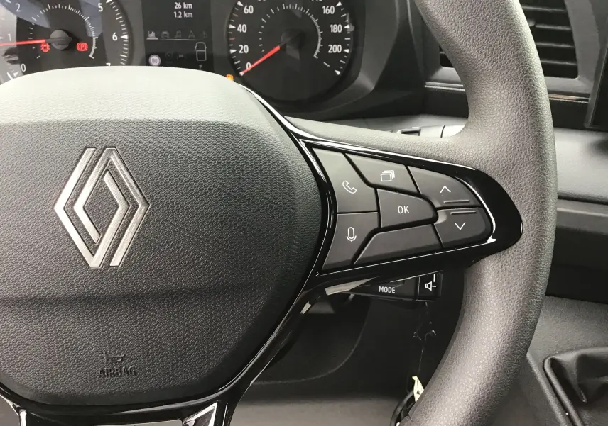 Gros plan sur le volant gris du Renault Master blanc 2025, avec commandes multifonctions et tableau de bord en arrière-plan.