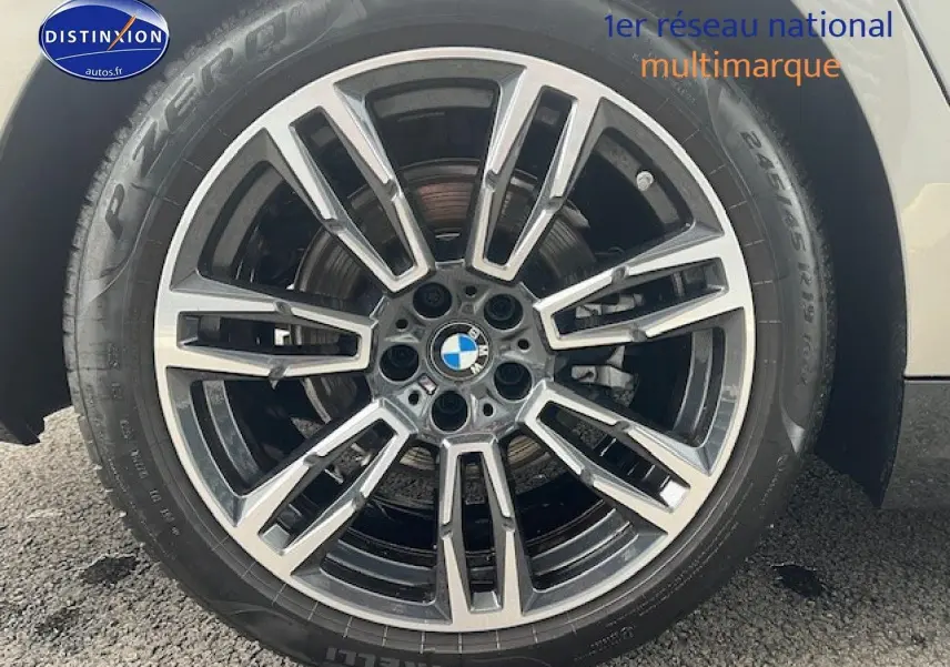 Gros plan sur la jante alu BMW avec logo central, montée sur pneu Pirelli, partie avant droite du véhicule gris visible.