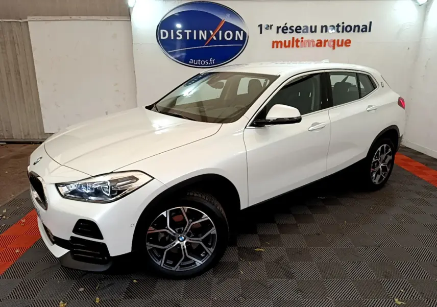 BMW X2 blanc en 3/4 avant droit dans un showroom, mettant en valeur ses phares LED et jantes design.