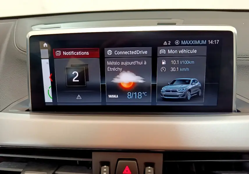 Écran central du tableau de bord BMW X2 2023 affichant météo, notifications et consommation, vue intérieure frontale.