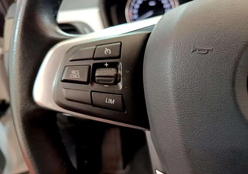 Gros plan sur les commandes du volant à gauche d'une BMW X2 blanche, avec boutons de régulateur de vitesse visibles.