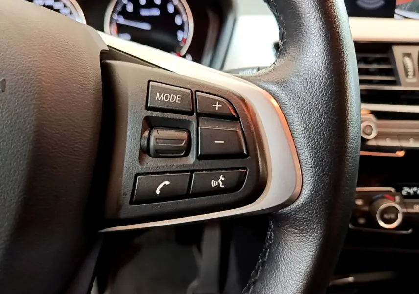 Gros plan sur les commandes du volant cuir noir de la BMW X2 2023, avec tableau de bord et écran en arrière-plan.