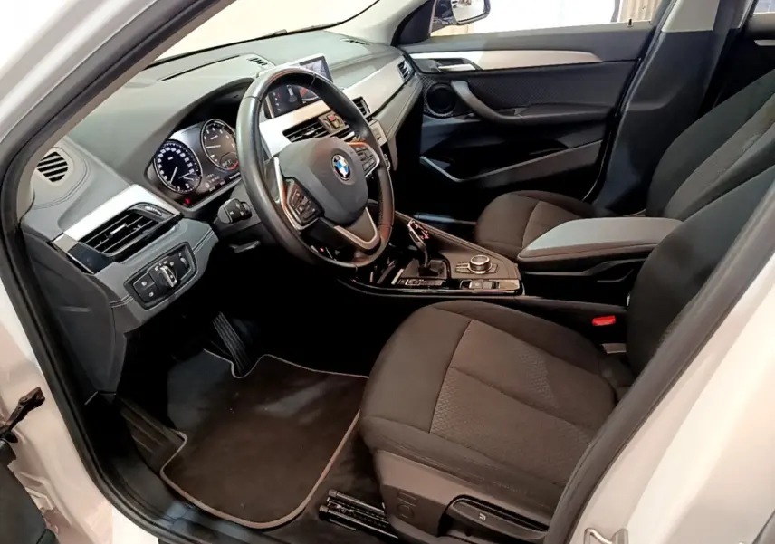 Intérieur côté conducteur de BMW X2 blanc 2023, volant cuir multifonctions et tableau de bord digital visible.