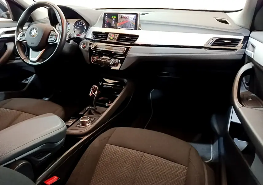 Intérieur BMW X2 sDrive18i 2023 vu côté passager, tableau de bord noir avec écran central et volant cuir multifonctions.