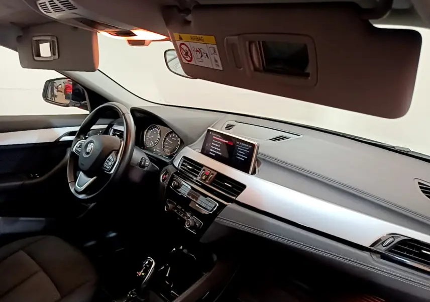 Vue intérieure côté conducteur du tableau de bord et volant cuir d'une BMW X2 sDrive18i blanc 2023.