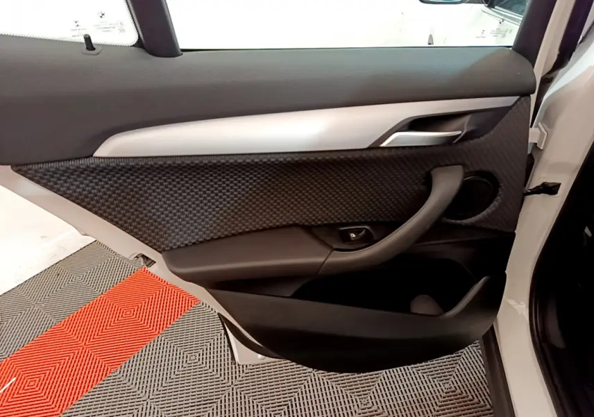 Gros plan sur la porte avant droite blanche d'une BMW X2 2023, avec habillage noir texturé et poignée intégrée.