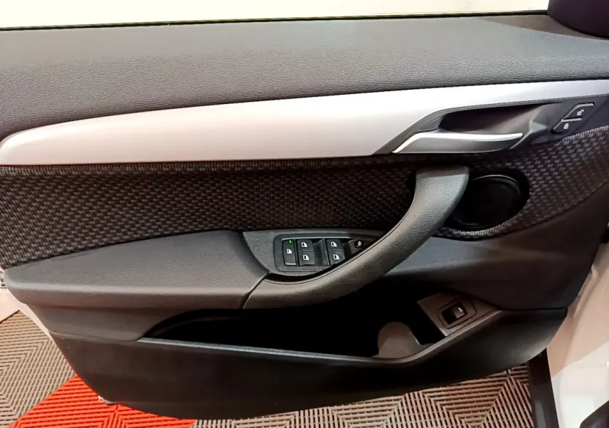 Gros plan sur la porte côté gauche de la BMW X2 blanche, montrant les commandes de vitres et la poignée intérieure noire.