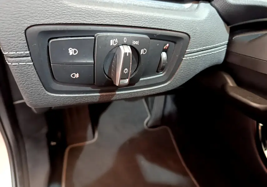 Gros plan sur le bouton de commande des phares sur la gauche du tableau de bord noir du BMW X2 blanc 2023.