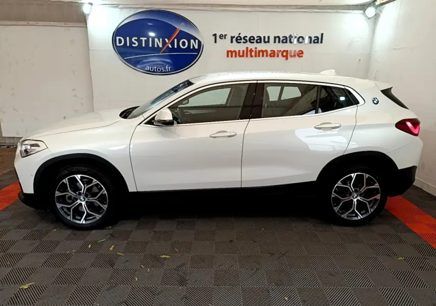 Profil côté gauche d'un BMW X2 blanc 2023 avec jantes alliage et feux arrière LED allumés en intérieur showroom