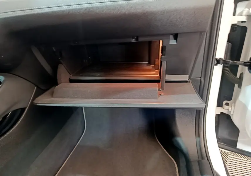Gant de boîte à gants ouvert côté passager d'un BMW X2 blanc, montrant l'intérieur éclairé et le tapis noir.