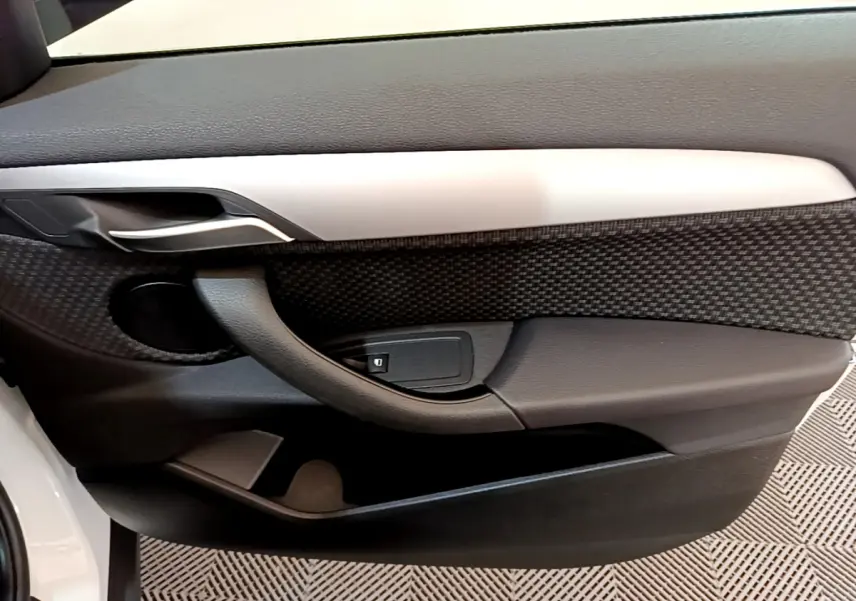 Gros plan sur la porte côté gauche intérieure du BMW X2 blanc, avec poignée et bouton de verrouillage visibles.