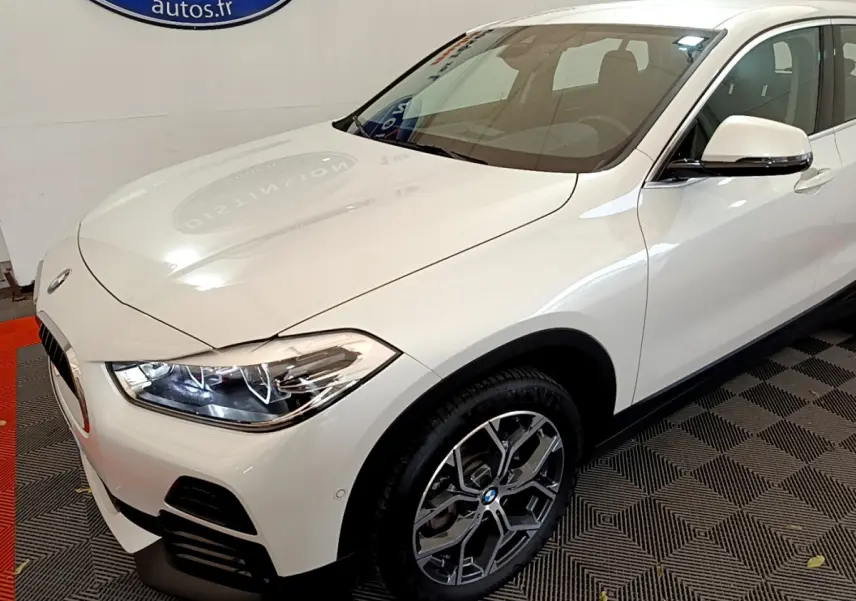 BMW X2 blanc en vue 3/4 avant droit, avec phares LED allumés et jantes alliage distinctives.