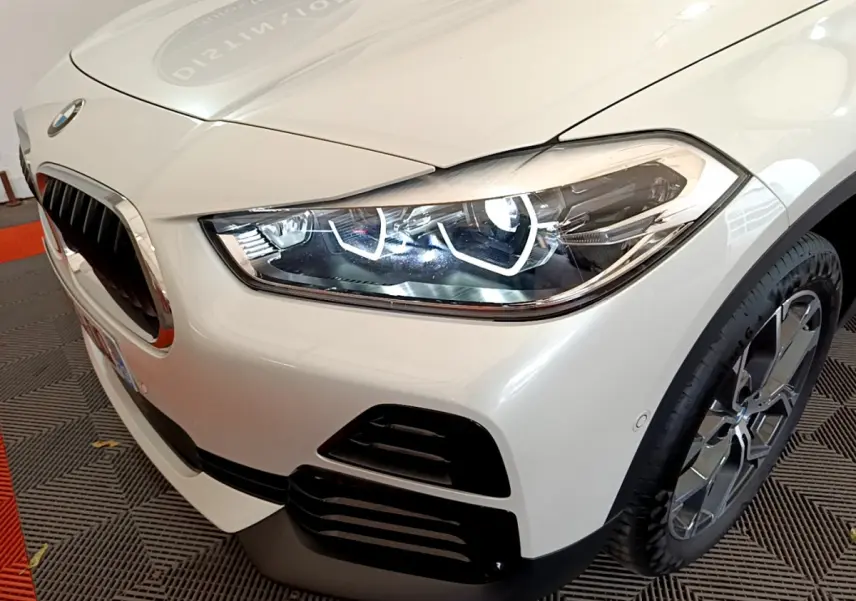 Gros plan sur l'avant droit d'un BMW X2 blanc 2023, mettant en valeur son phare LED et la calandre caractéristique.