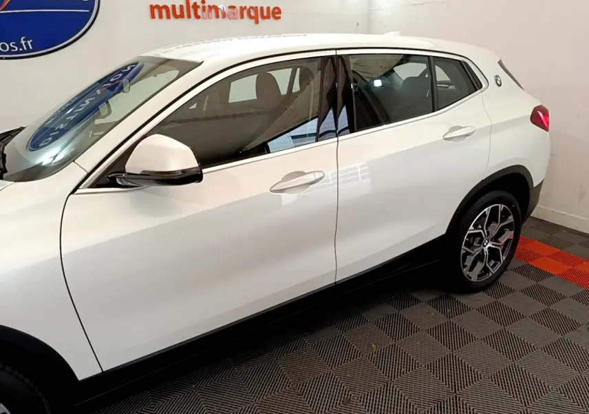Vue latérale côté gauche d'un BMW X2 blanc 2023 avec jantes alliage et rétroviseurs blancs sur sol damier.