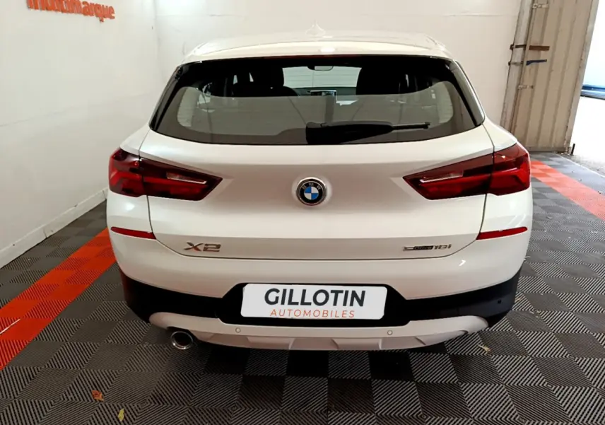 Vue arrière d'un BMW X2 blanc sDrive18i Business DesignDKG7 avec feux LED et sortie d'échappement visible.
