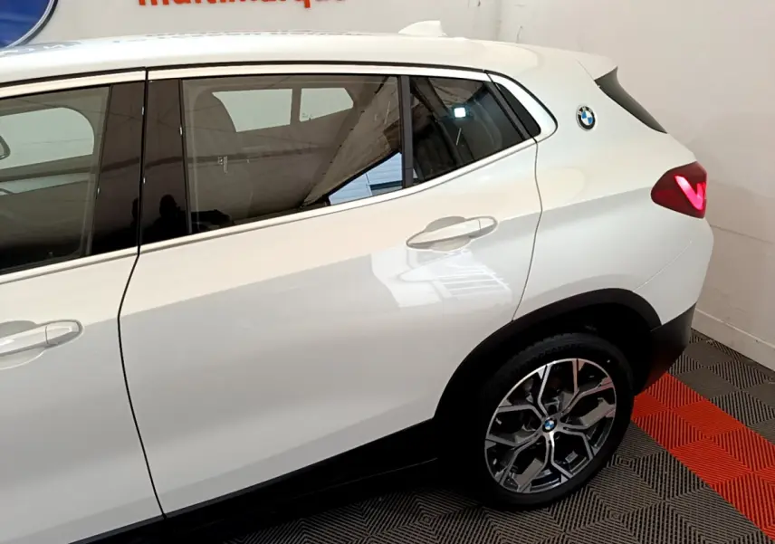 Vue latérale droite du BMW X2 blanc 2023, mettant en valeur la porte arrière, la jante alliage et le logo rond sur l'aile arrière.