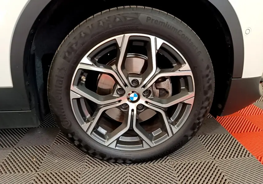 Gros plan sur la roue avant droite d'un BMW X2 blanc, avec jante alliage au design moderne et logo central visible.