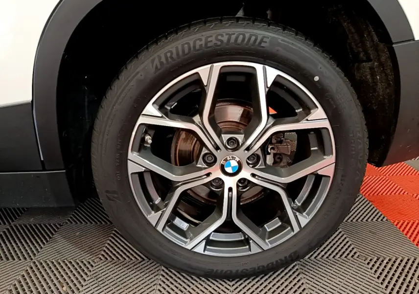 Gros plan sur la roue avant droite d'un BMW X2 blanc, mettant en valeur la jante alliage et le pneu Bridgestone.