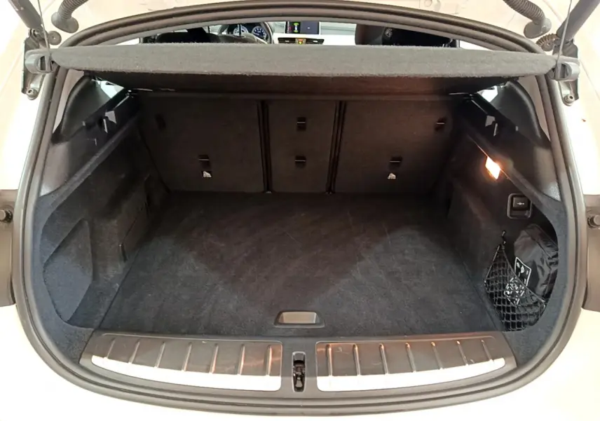Coffre ouvert vu de l'arrière d'un BMW X2 blanc, avec tapis noir et éclairage intérieur à droite.