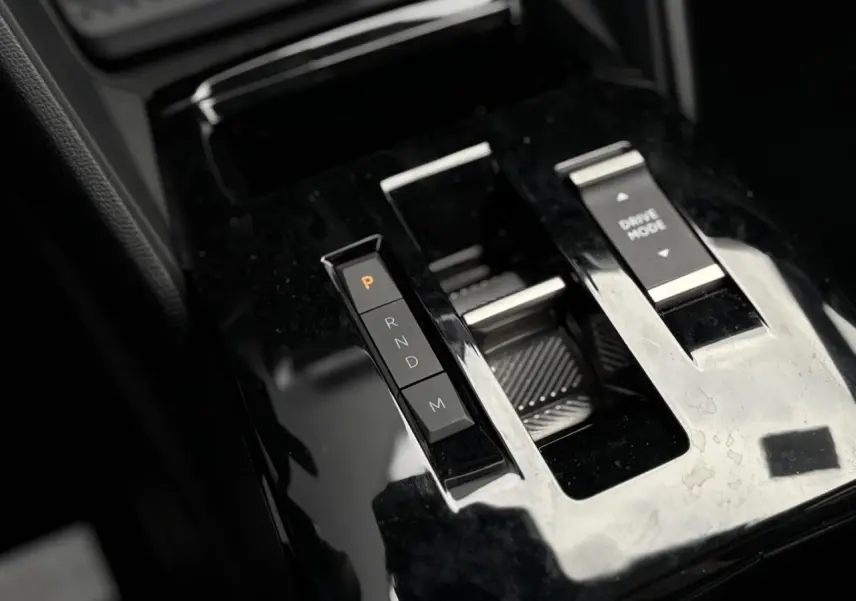 Gros plan sur la console centrale noire brillante de la Citroën C4 Hybrid 2025 avec sélecteur de boîte auto et bouton Drive Mode.