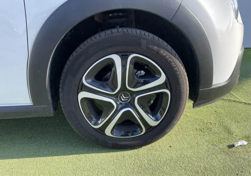 Gros plan sur la roue avant gauche d'une Citroën C3 blanche avec enjoliveur 3D noir et chrome satin.