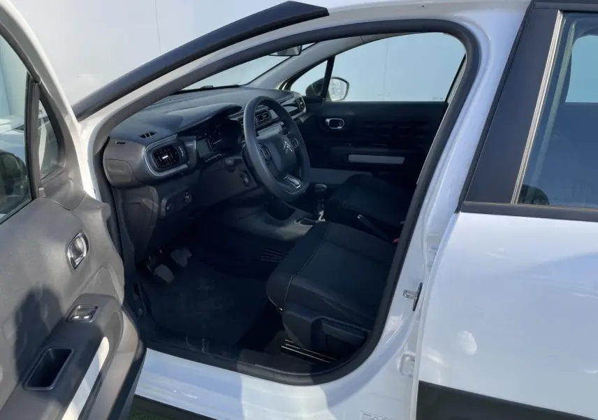 Intérieur côté conducteur d'une Citroën C3 blanc banquise 2024, montrant tableau de bord et sièges noirs.