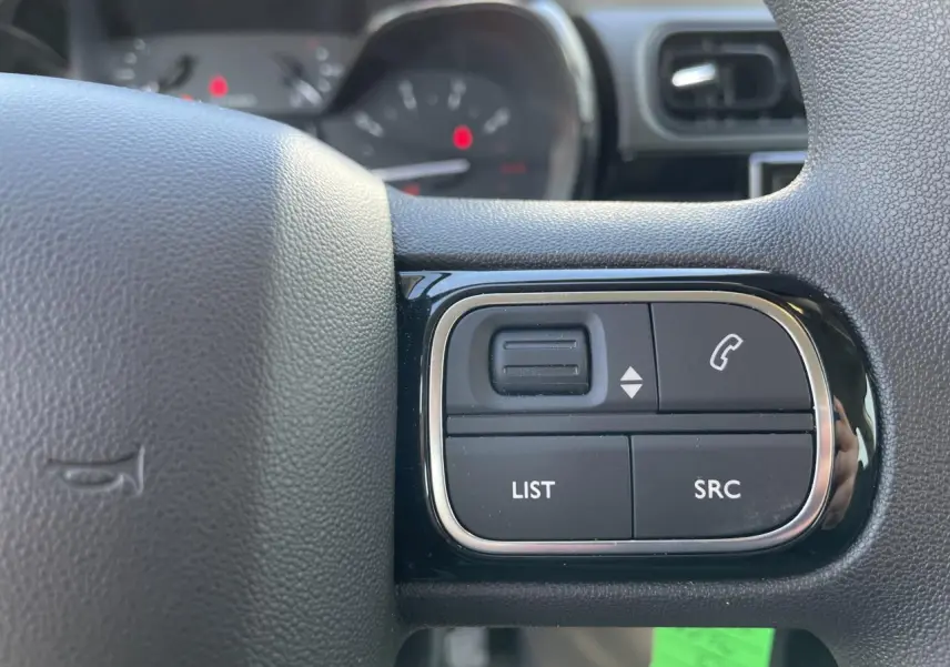 Gros plan sur les commandes audio au volant noir brillant de la Citroën C3 blanche, avec tableau de bord flou en arrière-plan.