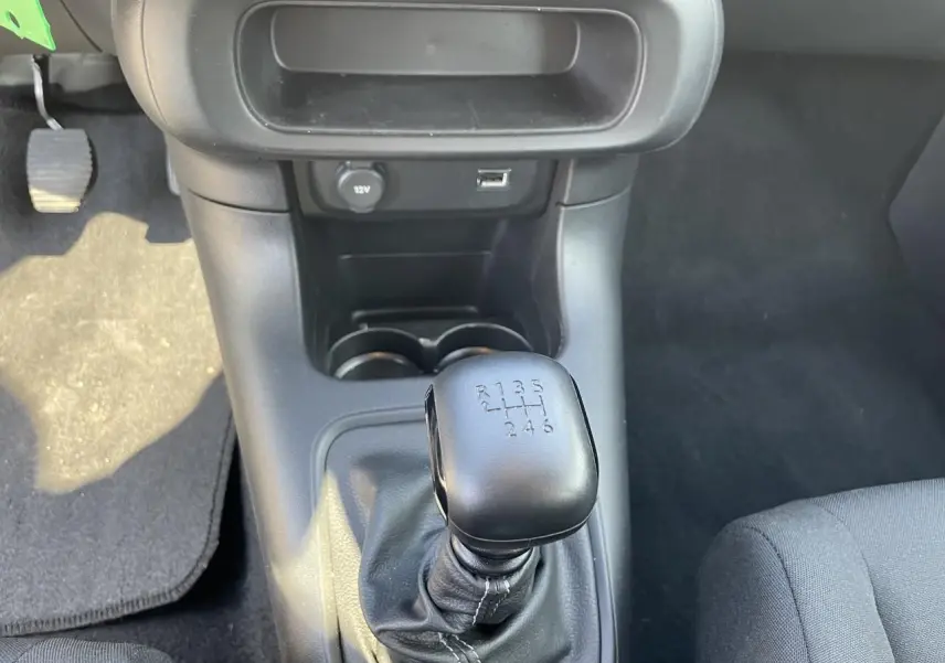 Le levier de vitesses manuel noir de la Citroën C3 blanche, vu de dessus dans l'habitacle.