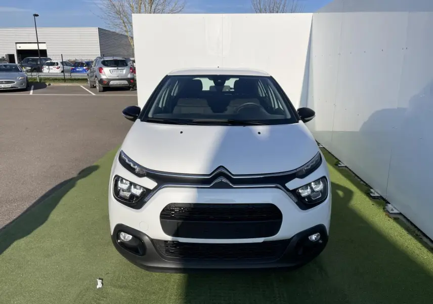 Vue frontale d'une Citroën C3 blanche Banquise avec calandre noire et feux LED distinctifs sur fond urbain.