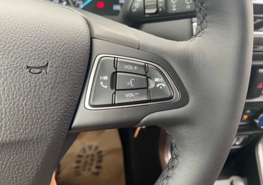 Gros plan sur les commandes audio au volant du Ford EcoSport 2022, cuir noir et tableau de bord en arrière-plan.