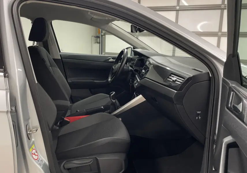Intérieur avant droit d'une Volkswagen Polo 2023 argent, montrant sièges noirs et tableau de bord moderne.