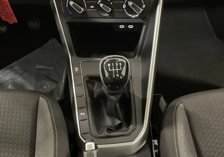 Le levier de vitesses manuel noir au centre de la console d'une Volkswagen Polo 2023 avec sièges gris.