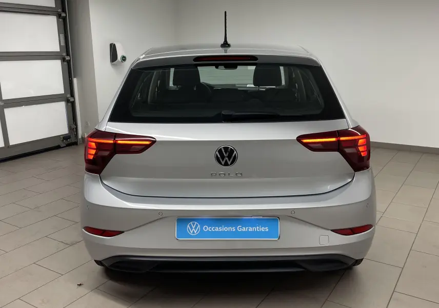 Vue arrière d'une Volkswagen Polo 2023 en peinture métallisée reflet d'argent avec feux arrière allumés dans un garage.