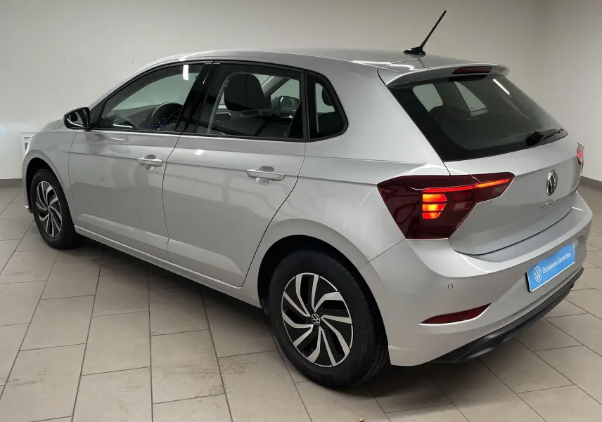 Volkswagen Polo 1.0 TSI 95 Life en reflet d'argent vue 3/4 arrière droit avec feux allumés en intérieur showroom.