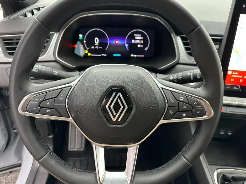 Vue rapprochée du volant multifonction noir avec logo Renault, tableau de bord numérique et écran tactile partiel du Renault Captur 2025.