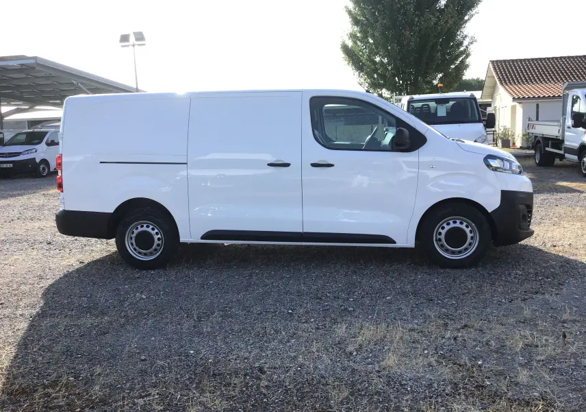 Profil droit d’un utilitaire blanc Citroën Jumpy XL 2.0 BlueHDi 120 Premium 3 places, stationné sur un sol gravillonné.