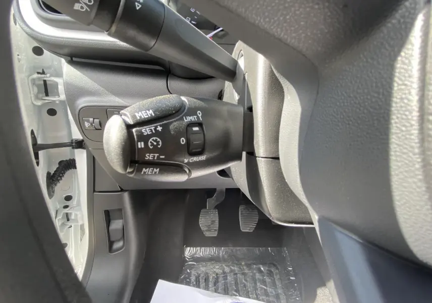 Vue rapprochée sous le volant de la Citroën C3 blanche 2022, montrant les commandes du régulateur de vitesse et les pédales.