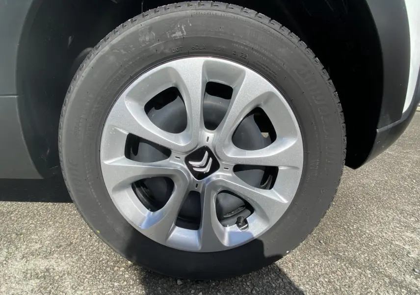 Gros plan sur la roue avant droite de la Citroën C3 blanche 2022 avec enjoliveur argenté à cinq branches arrondies.