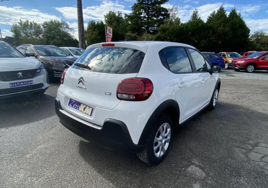 Vue 3/4 arrière droite d'une Citroën C3 blanche 2022 avec enjoliveurs 15 pouces et vitrage teinté arrière.