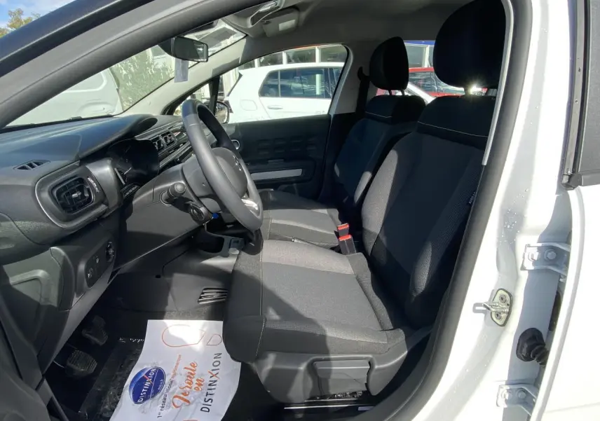 Intérieur avant de la Citroën C3 blanche 2022, montrant les sièges tissu gris et le tableau de bord côté conducteur.