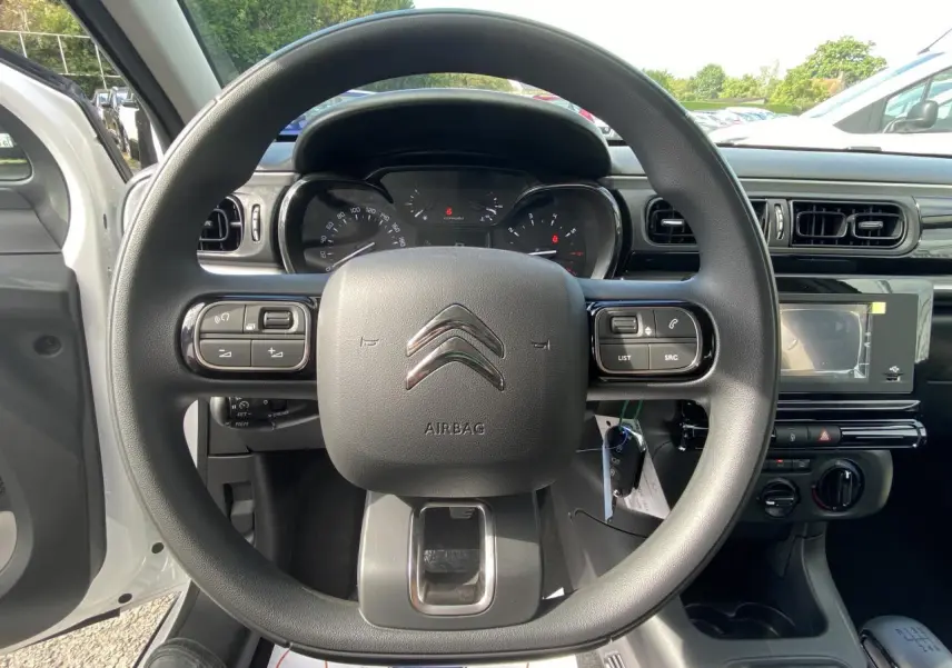 Vue depuis le siège conducteur du tableau de bord et du volant noir d'une Citroën C3 blanche de 2022, avec commandes intégrées.
