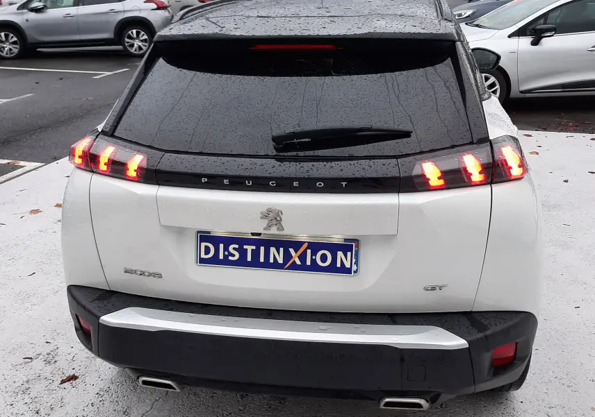 Vue arrière d'un Peugeot 2008 blanc nacré avec toit noir, feux arrière allumés et double sortie d'échappement chromée.