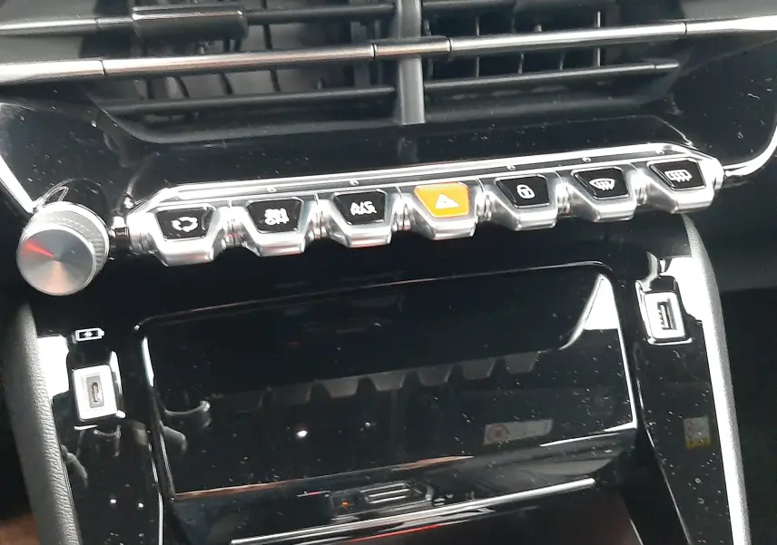 Vue rapprochée du tableau de bord noir brillant du Peugeot 2008 2023, mettant en valeur les commandes chromées et les aérateurs.