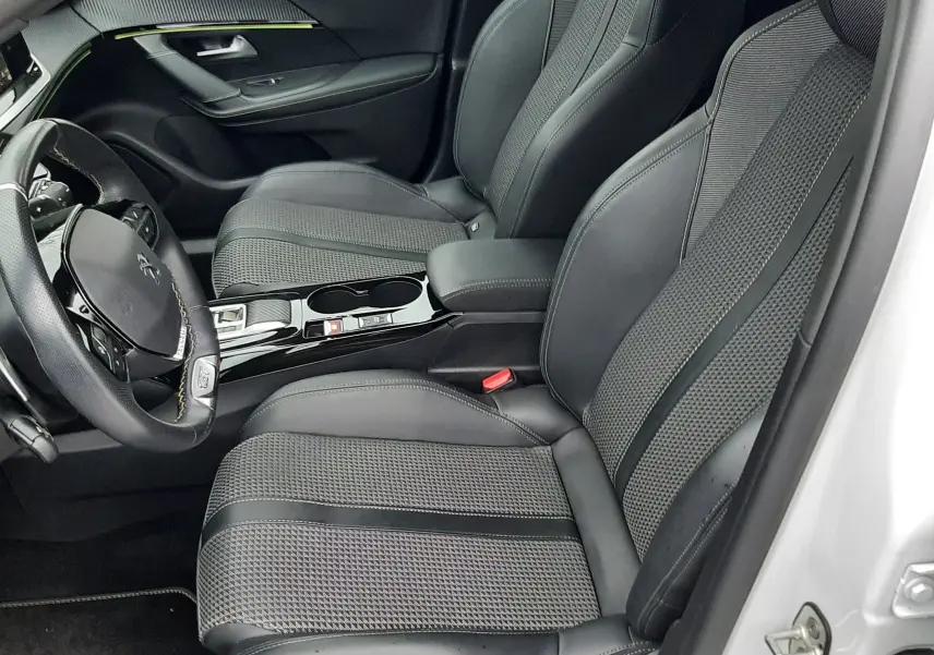 Vue intérieure côté conducteur du Peugeot 2008 2023 blanc nacré, sièges noirs en cuir et tissu avec console centrale brillante.
