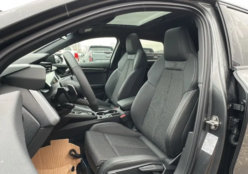 Vue intérieure côté gauche de l'Audi A3 TFSI 150 Hybrid S-Line 2025, sièges sport cuir tissu gris avec toit panoramique.